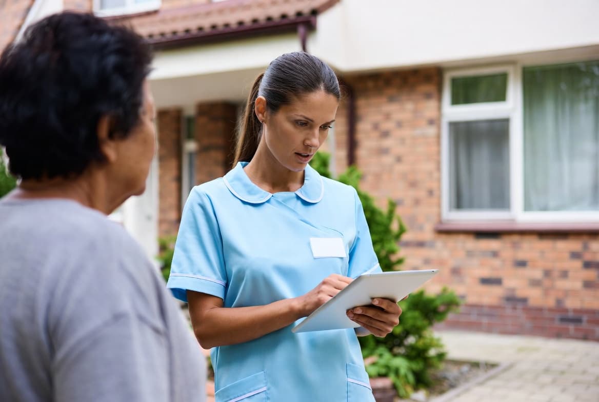 A home-care caregiver checking visit details on a tablet at a residential location — the operational moment of EVV sync.